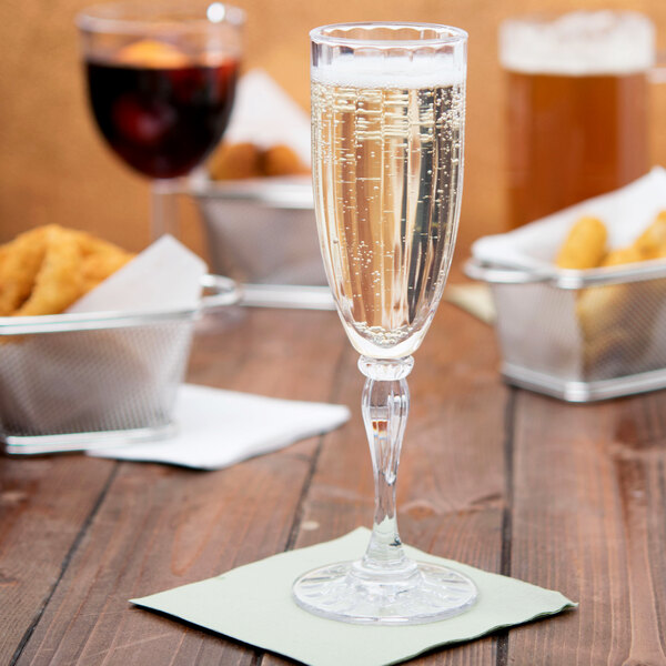 A close-up of a GET SAN plastic fluted champagne flute filled with champagne on a table.