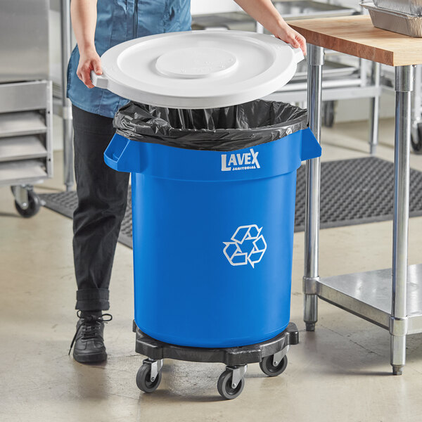 A woman pushing a blue Lavex recycling can with a white lid.