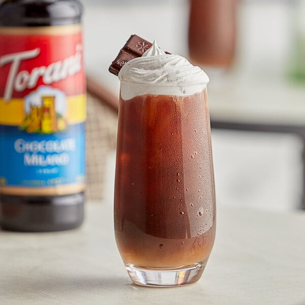 A glass of Torani Chocolate Milano flavoring syrup in chocolate milkshake with whipped cream and a chocolate bar.
