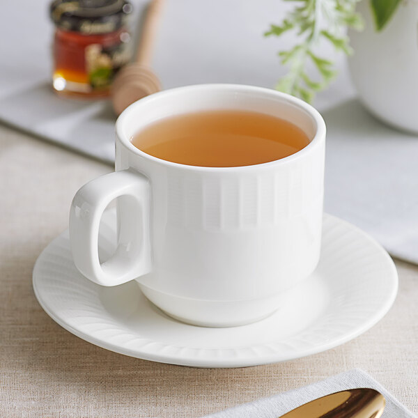 An Acopa Cordelia bright white porcelain cup filled with brown liquid on a saucer.