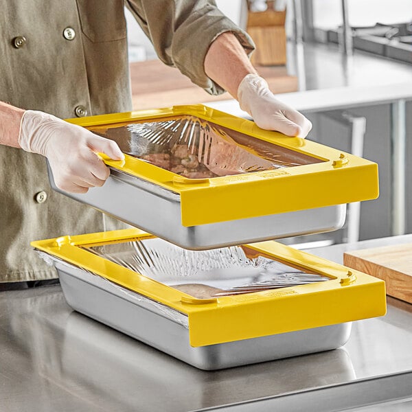 A person in gloves holding a yellow Pan Stacker container on a counter in a professional kitchen.