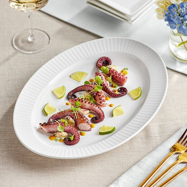 A white Acopa Cordelia porcelain platter with an embossed octopus on it holding octopus and lime slices.