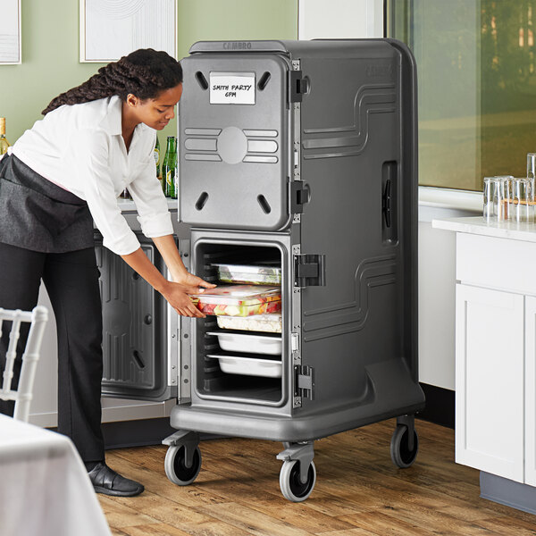 A woman loading food into a Cambro Pro Cart Ultra food pan carrier.