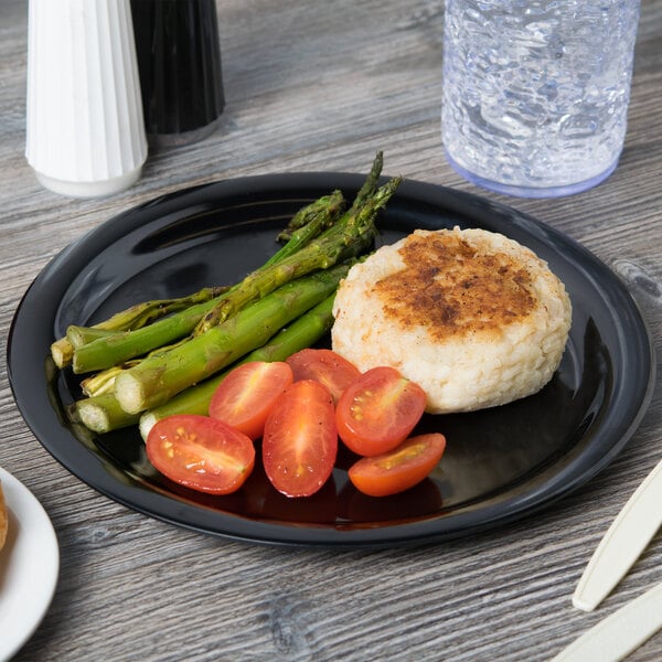 A Carlisle black melamine plate with a hamburger and asparagus on a table.