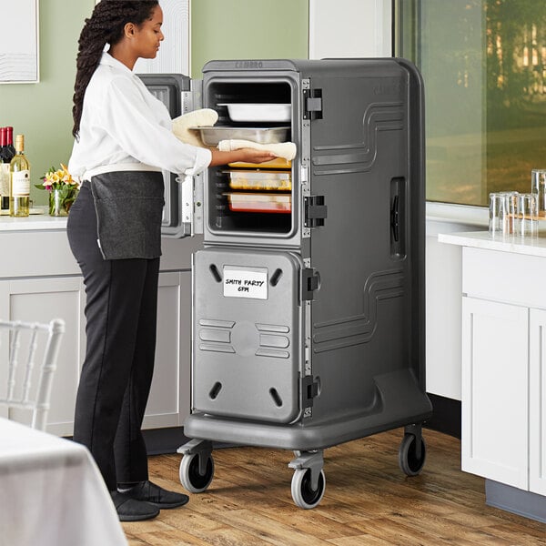 A woman putting food into a Cambro Pro Cart Ultra pan carrier.