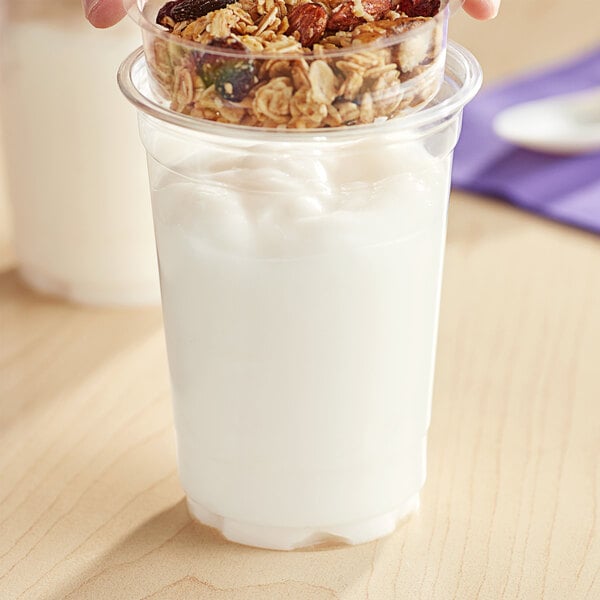 A hand holding a plastic cup of So Delicious plain coconut milk yogurt with granola.