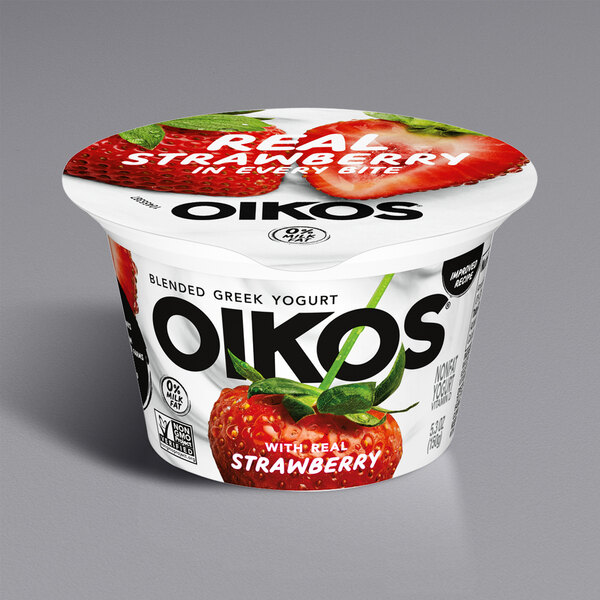 A close up of a container of Oikos Core Strawberry Greek Yogurt with strawberries on the bottom.