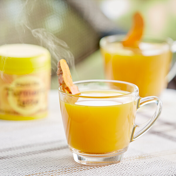A glass mug of orange David Rio Turmeric Latte on a table with a jar of the mix.