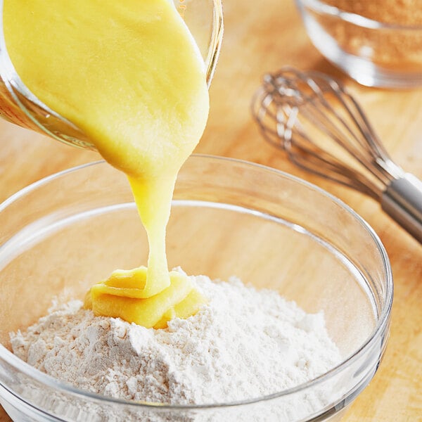 A bowl of flour with a yellow liquid being poured into it to make batter.