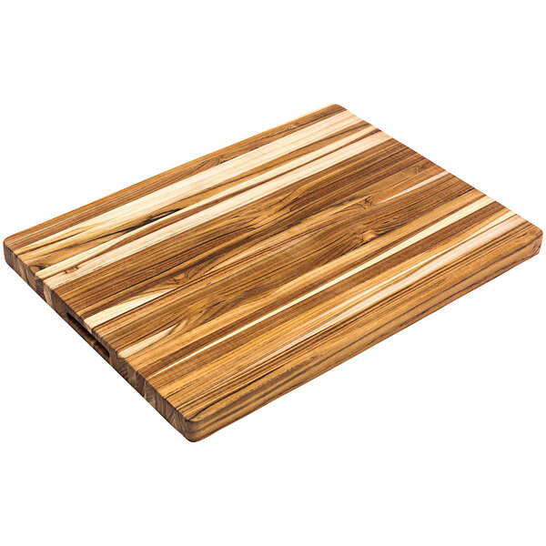 A Teakhaus edge grain teakwood cutting board with hand grips on a table.