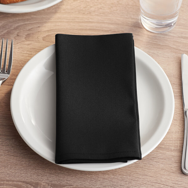 A white plate with a black Choice cloth napkin and silverware on a table.