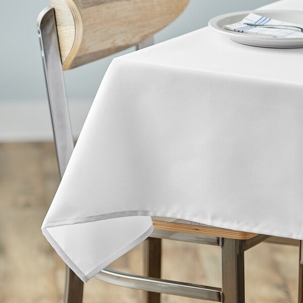 A table with a white Choice square tablecloth and a plate on it.