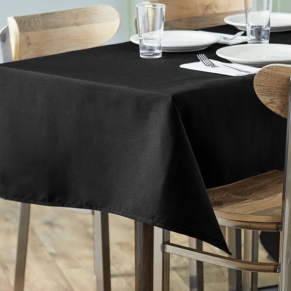 A table with a Choice black rectangular tablecloth and plates on it.