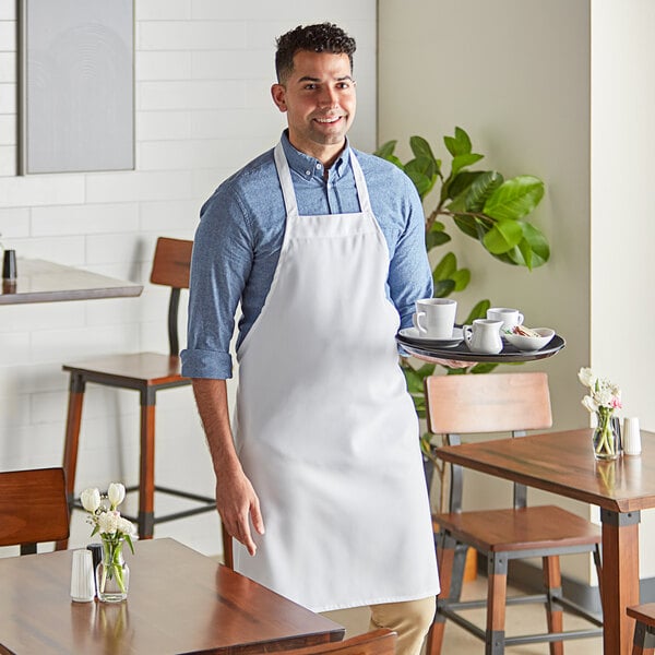 A man wearing a white Choice bib apron serving coffee on a wooden table.