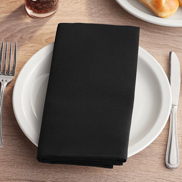 A white plate with a black Choice cloth napkin and silverware on it.