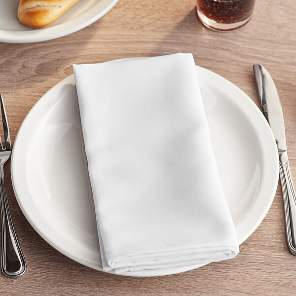 A white Choice cloth napkin folded on a plate with a fork and knife.