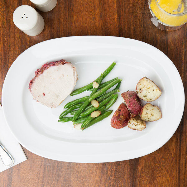 A white Arcoroc porcelain platter with meat, potatoes, and green beans on a table.