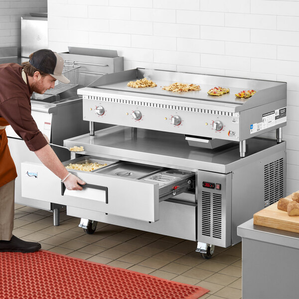 A man in an apron using a Cooking Performance Group electric countertop griddle over a refrigerated base.