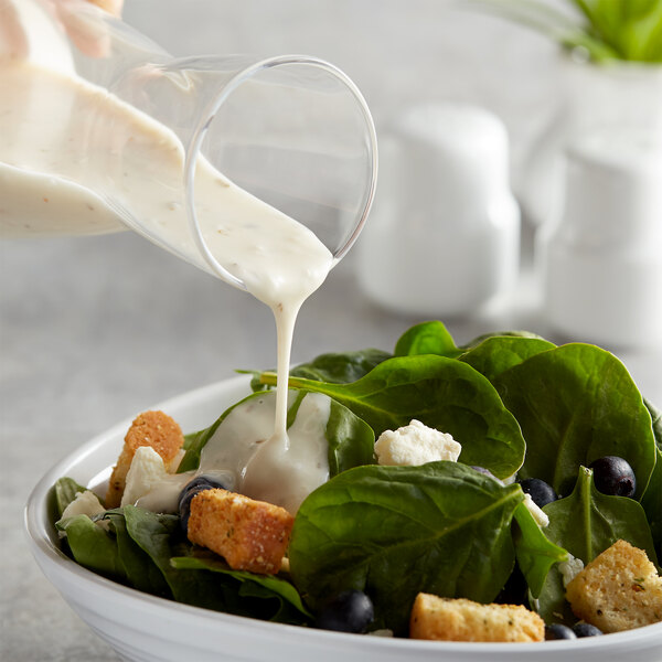 A person pouring AAK Select Creamy Italian Dressing from a glass container onto a spinach salad.