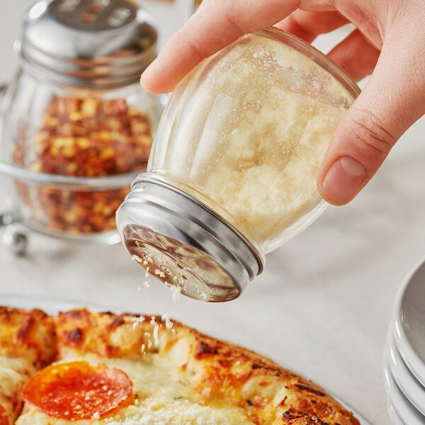 A hand using a Choice glass cheese shaker on a pepperoni pizza.