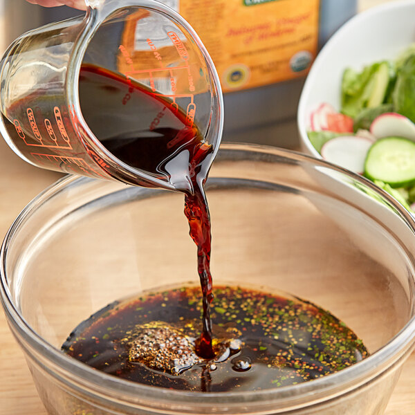 A person pouring Colavita Organic Balsamic Vinegar into a bowl of vegetables.