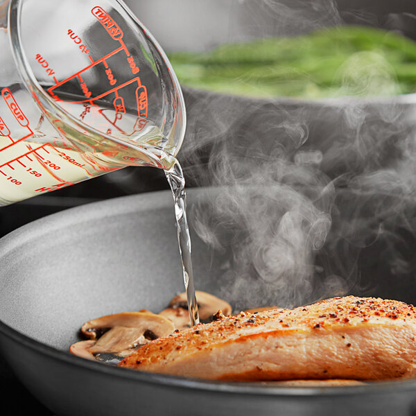 A person pouring Colavita White Balsamic Vinegar into a pan of food.