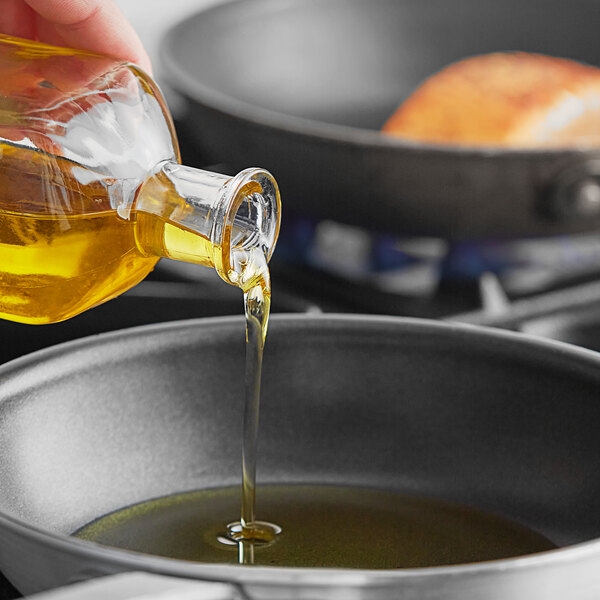A person pouring Colavita oil into a frying pan.