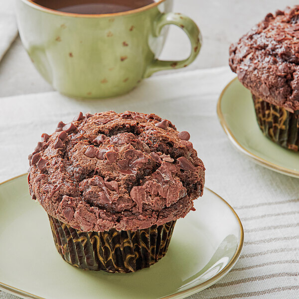 A David's Cookies double chocolate chip muffin on a green plate next to a cup of coffee.