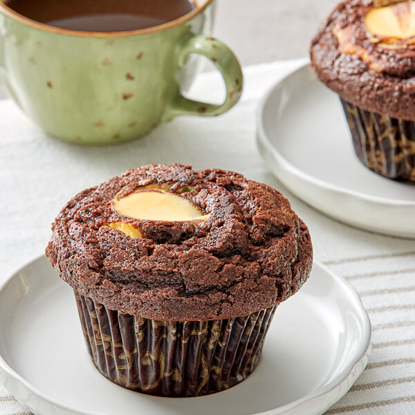 A chocolate muffin on a plate next to a cup of coffee.