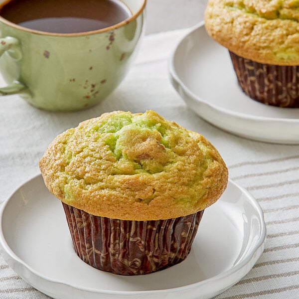 A David's Cookies pistachio muffin on a white plate with a cup of coffee.