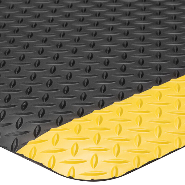 A close up of a Lavex black anti-fatigue mat with yellow diamond borders.
