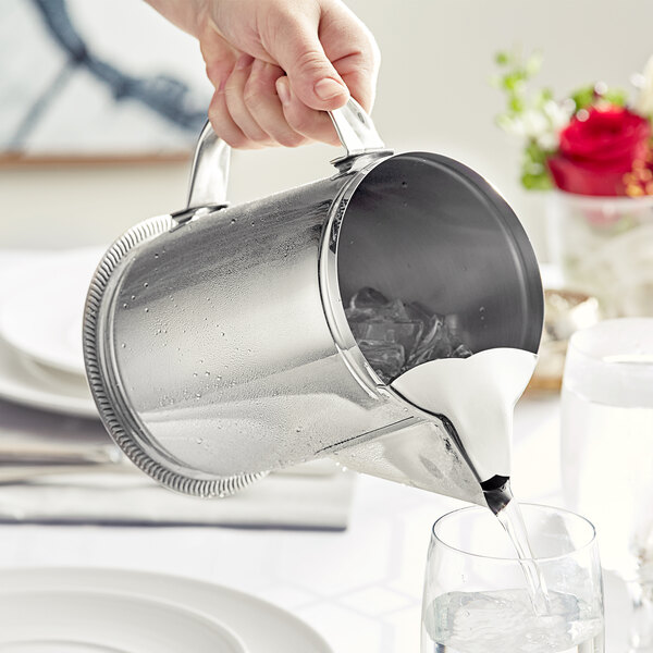 A hand pouring water into a stainless steel pitcher.