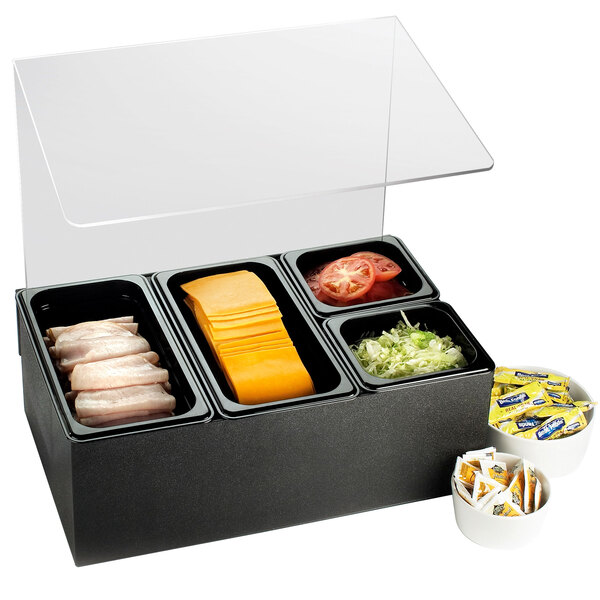A black container with four compartments of food on a table with a sneeze guard