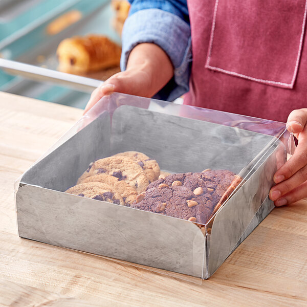 A person holding an Enjay Marble Laminated take-out box filled with cookies.