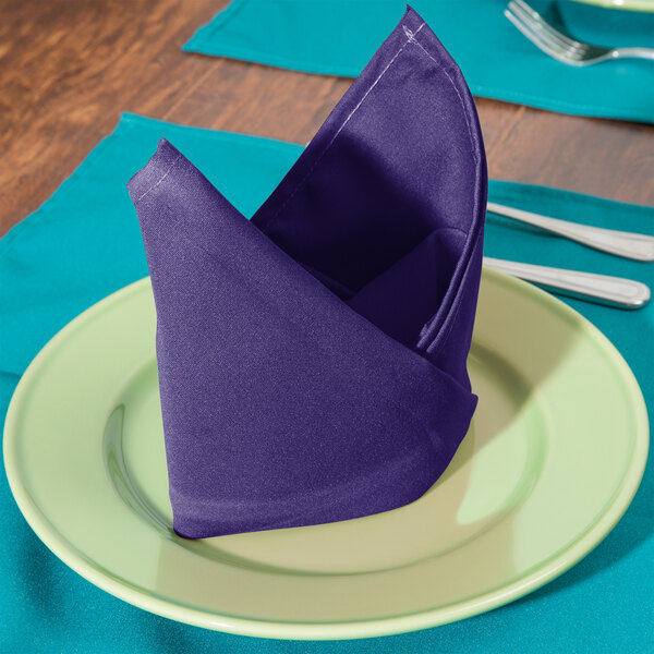 A folded purple Intedge cloth napkin on a plate with silverware.