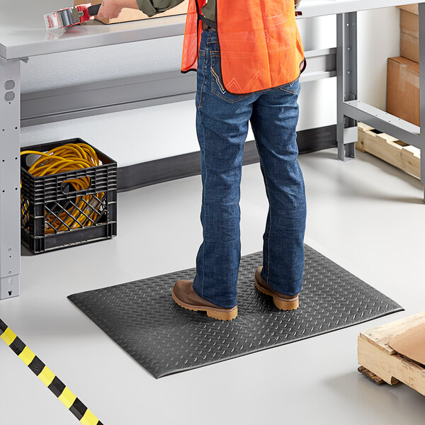 A man in a construction vest standing on a black anti-fatigue mat.