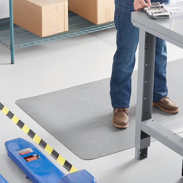 A man standing on a Lavex K-Marble Foot anti-fatigue mat in a warehouse.