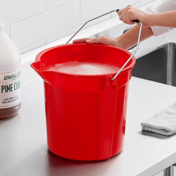 A woman using a red Lavex round bucket to wash dishes in a professional kitchen.