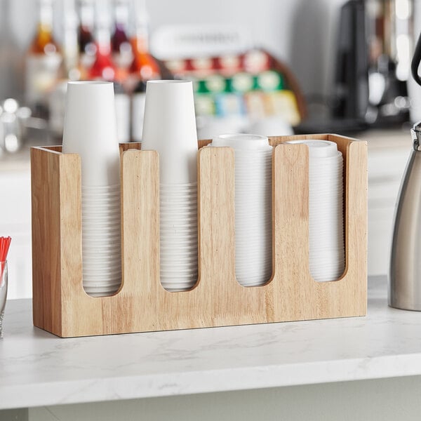 A white wooden Acopa 4-section cup and lid organizer on a wooden counter.