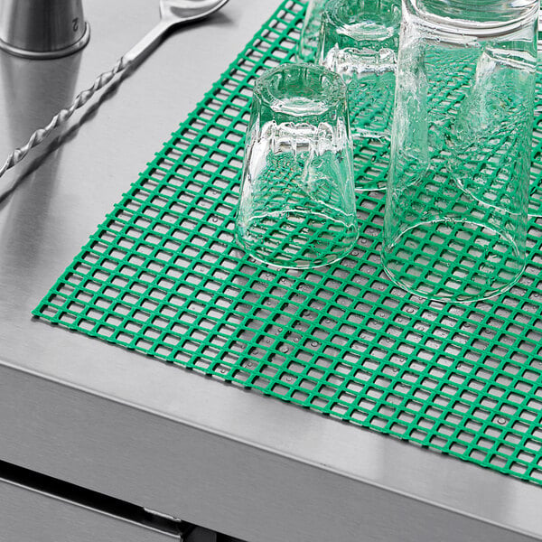 A group of glasses on a green mesh shelf liner.