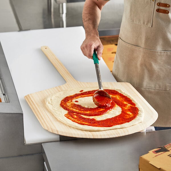 A man using a Choice wooden pizza peel to spread sauce on a pizza.
