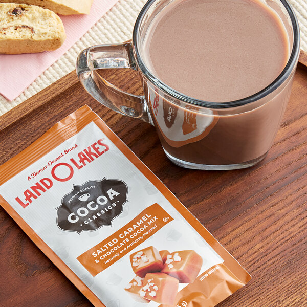 A glass mug of Land O Lakes Salted Caramel and Chocolate hot cocoa next to a packet of Land O Lakes Salted Caramel and Chocolate hot cocoa.