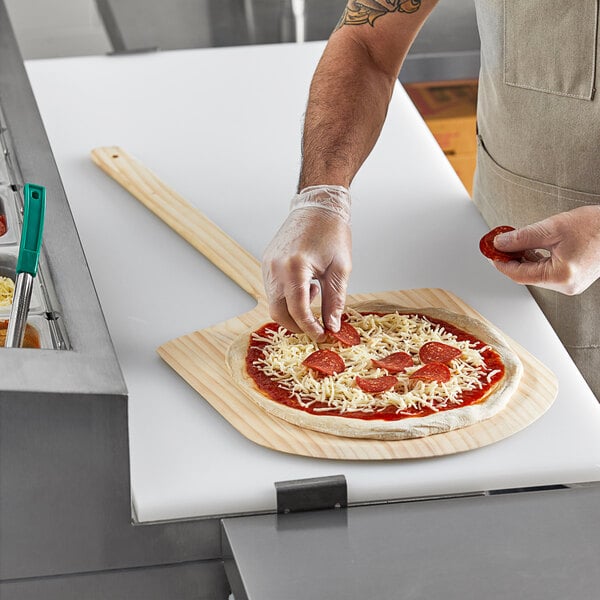 A person using a Choice wooden pizza peel to transfer a pizza to a cutting board.