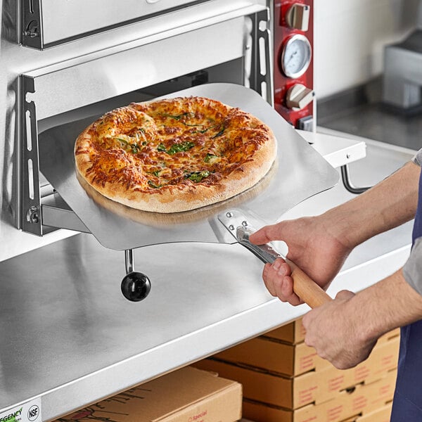 A person using a Choice aluminum pizza peel to remove a pizza from an oven.