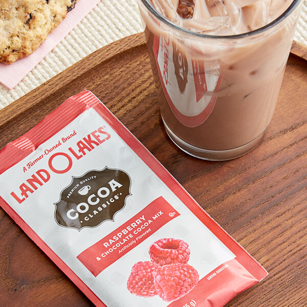 A cup of Land O Lakes raspberry and chocolate hot cocoa next to a cookie on a table.