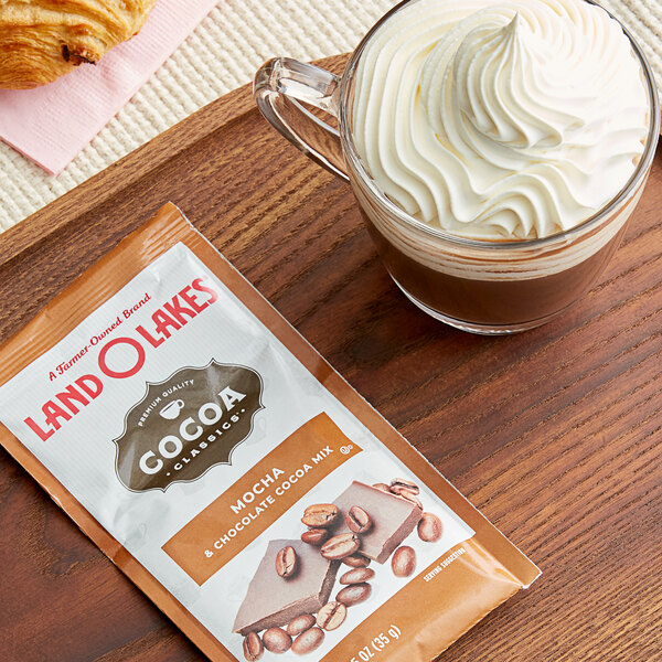 A cup of hot chocolate with whipped cream and a packet of Land O Lakes Cocoa Classics Mocha and Chocolate.