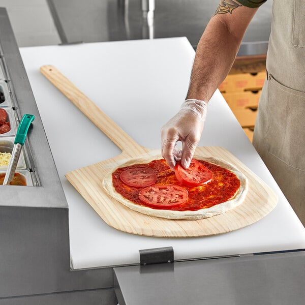 A man using a Choice wooden pizza peel to remove a pizza from a pizza oven.