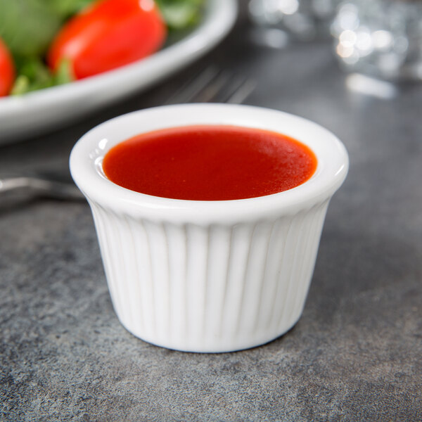 A Tuxton white fluted ramekin filled with red sauce.