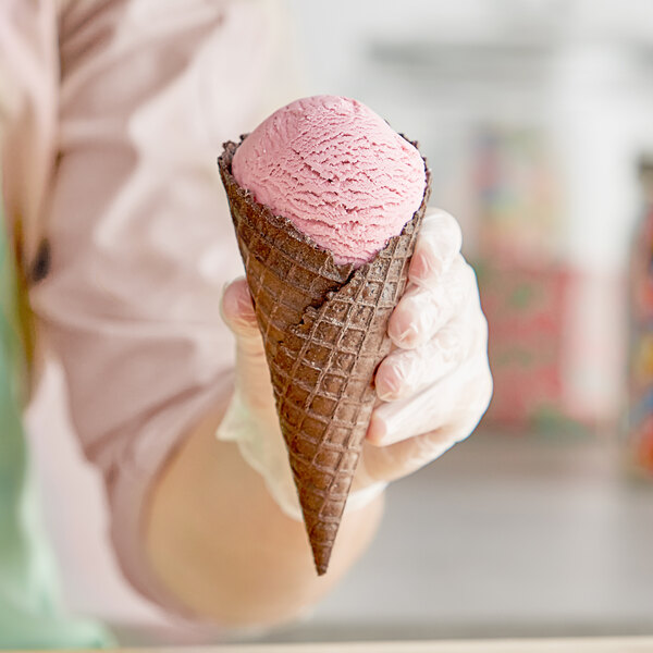 A person holding a JOY Cookies & Creme Waffle Cone with a pink jacket.