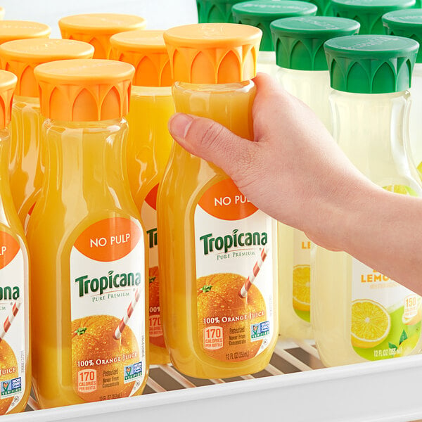 A hand holding a yellow Tropicana No Pulp Pure Premium Orange Juice bottle.